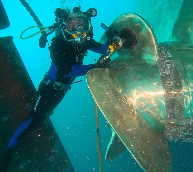 Professional diver polishing a ship propeller underwater